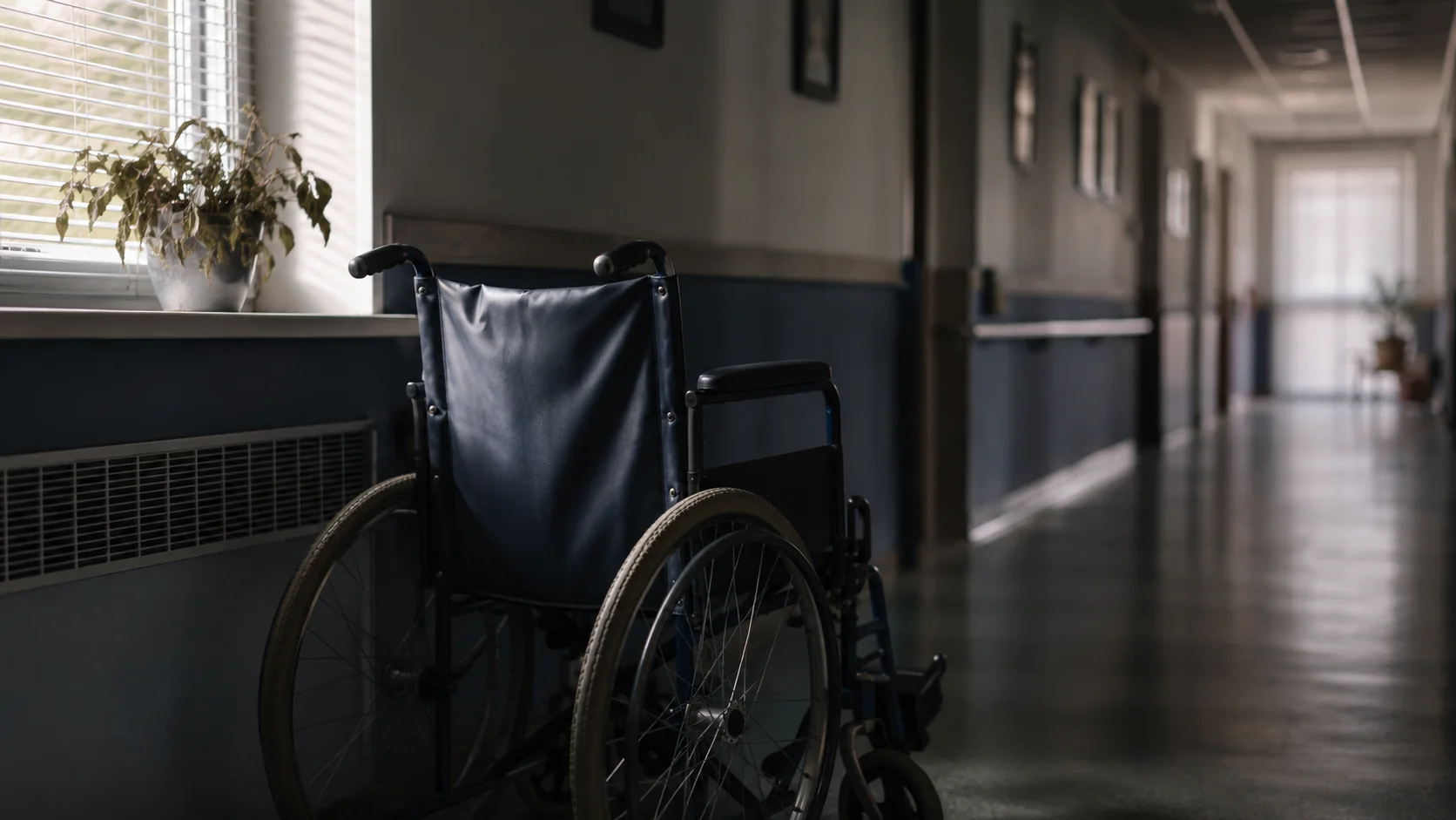 An empty wheelchair beside a window in a quiet nursing home corridor