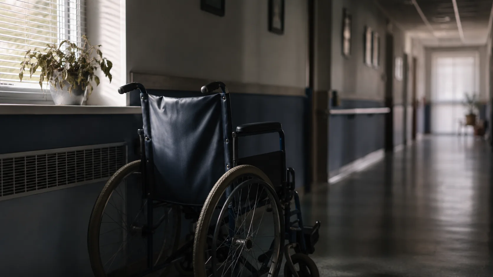 Empty wheelchair beside a window in a quiet nursing home corridor